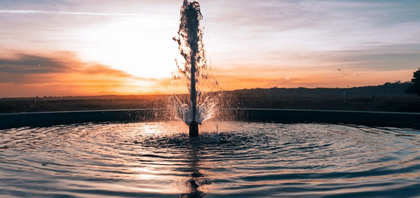 Fountain in a tranquil setting with sunset colors in the background.