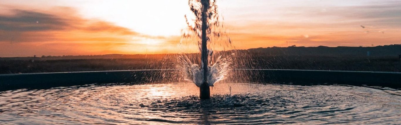 Fountain water splashing at sunset, creating ripples in a tranquil pool.