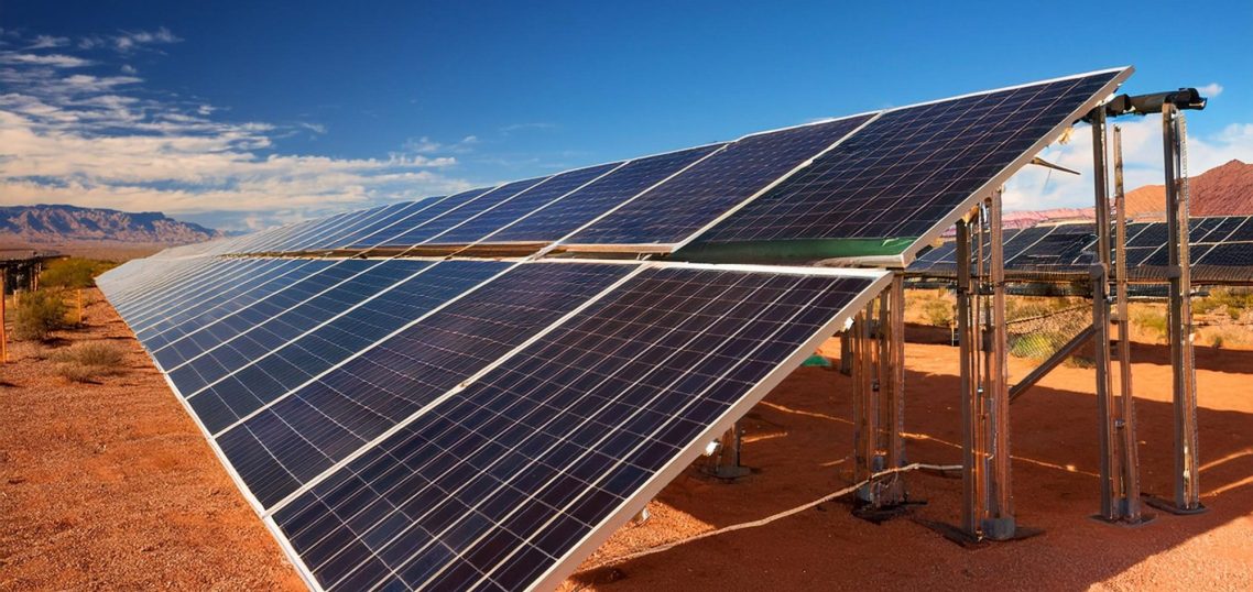 Solar panels installed in a desert landscape under a clear blue sky.
